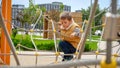 Little boy climbing through obstacles of ropes and nets on new public playground. Active child, sports and development, kids Royalty Free Stock Photo