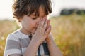 Little Boy closed her eyes, praying in a field wheat. Hands folded in prayer