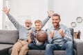 Little boy on couch with grandfather and father, cheering for a basketball game and holding a Royalty Free Stock Photo