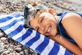 The little boy in diving goggles lying on a Striped blue and white beach towel and smiling Royalty Free Stock Photo