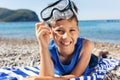 The little boy in diving goggles lying on a Striped blue and white beach towel and smiling happily Royalty Free Stock Photo