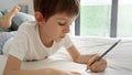 Little boy doing his homework in bed, writing in a notebook with diligence and dedication. Importance of education and child