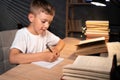 Little boy doing homework at home late in evening, schoolboy writes a test with a pen in a notebook while sitting at a Royalty Free Stock Photo