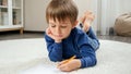 Little boy doing homework and writing in copybook on floor at home. Concept of domestic education and child development. Royalty Free Stock Photo