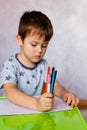 Little boy drawing with color pencils. There are many colored pencils in the boy`s hands. Small boy draws at the table