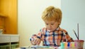 Little boy on drawing lesson. Serious kid enjoy painting with brush and colours wearing colourful shirt. Young child