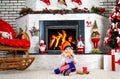 Little boy dressed like christmas elf sitting near the Christmas tree by the fireplace,eating cookies and drinking milk. Royalty Free Stock Photo