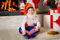 Little boy dressed like christmas elf sitting near the Christmas tree in the fireplace room. Royalty Free Stock Photo