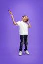 Little boy dressed modern casual outfit playing with grogger toy and talking on phone against purple studio background.