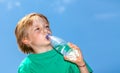 Little boy drinking water from a bottle against a blue sky Royalty Free Stock Photo