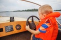 Little boy driving a motor boat firmly holding the steering whee