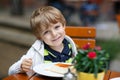 Little boy eating cake in outdoor cafe. Royalty Free Stock Photo