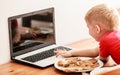 Little boy eating meal while using laptop computer at home Royalty Free Stock Photo