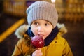 Little boy eating red apple covered in caramel on Christmas market. Traditional child& x27;s enjoyment and fun during Xmas time Royalty Free Stock Photo