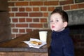 Little boy eating sausage roll and a cup of coffee