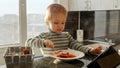 Little boy eating soup and watching video on tablet computer. Domestic food, gadget addiction, children healthy nutrition Royalty Free Stock Photo