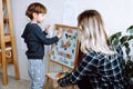 Little boy and educator playing and studying numbers, letters and alphabet on magnetic board in playroom backview