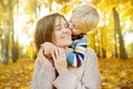 Little boy embraces his young mother and kissing her during stroll at sunny autumn park Royalty Free Stock Photo