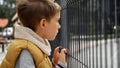 Little boy feeling sad and alone looking through metal fence on children playground. Child depression, problems with bullying, Royalty Free Stock Photo