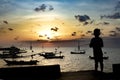 Little boy fishes on a pier in a rustic port. Silhouette of a boy at sunset, holding a fishing pole and looking at the setting sun Royalty Free Stock Photo