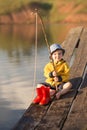 A little boy fishing and wants to catch the biggest fish. Little boy siting on wooden dock and fishing at sunset. Royalty Free Stock Photo