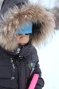 Little boy in fluffy hat playing in snow sad