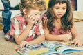 Little Caucasian curly boy and girl lying on the floor and reading an illustrated book.