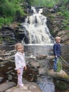 Little boy and girl relaxing and enjoying beautiful view on vacation hiking trip at waterfall. Travelling with kids concept