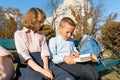 Little boy and girl schoolchildren read a book, sit on a bench, children with backpacks, bright sunny autumn day Royalty Free Stock Photo