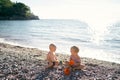 Little boy and girl sitting with toy molds on a pebble beach Royalty Free Stock Photo