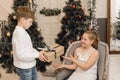 Little boy gives a cute girl a Christmas present in a bright interior against the background of a Christmas tree. A Royalty Free Stock Photo