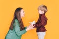 A little boy gives his mother a bouquet of flowers and covers her eyes with his hand against a yellow background Royalty Free Stock Photo