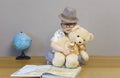 A little boy in glasses and a hat sits on the floor and hugs a teddy bear. Royalty Free Stock Photo