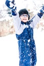 Little boy with glasses in winter jumpsuit throws snow