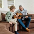 Little boy grandson watching how grandad playing on acoustic guitar while sitting together on sofa in the living room Royalty Free Stock Photo