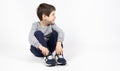 Little boy in a gray sweatshirt, blue sweatpants and sneakers on a white background sits and looks away, space for text Royalty Free Stock Photo