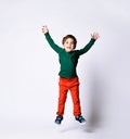 Little boy in green jumper, orange pants, blue sneakers. He jumping with raised hands, smiling, posing isolated on white Royalty Free Stock Photo