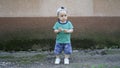 Little boy in green T-shirt and hat alone near plastered wall