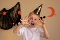 A little boy in a Halloween cap makes a scary frightening face on Halloween. Hands raised, halloween themed background