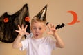 A little boy in a Halloween cap makes a scary frightening face on Halloween. Hands raised, halloween themed background