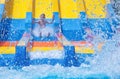 Little boy with hands up enjoys ride on water slide splashing water in aqua park