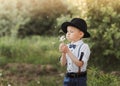 A little boy in a hat blowing on a white dandelion. Child in retro clothing Royalty Free Stock Photo