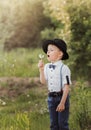 Little boy in a hat blowing on a white dandelion. Child in retro clothing. Vertical Royalty Free Stock Photo