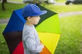 Little boy in hat with multicolor umbrella in park after rain on sunny summer day Royalty Free Stock Photo