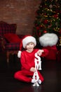 Little boy in hat red Santa sit on floor by Christmas tree and playing wooden letters Xmas. Happy small boy decorated festive livi Royalty Free Stock Photo