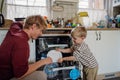 Little boy helping father to load dishwasher after breakfast. Cleaning the kitchen before leaving to work and daycare Royalty Free Stock Photo