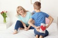 Little boy hiding handmade card for mother behind his back in bedroom Royalty Free Stock Photo