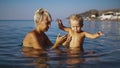 Little boy and his blond mom goes into water to swim and playing in the sea