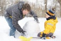 Little boy with his father building snowman in snowy park. Active outdoors leisure with children in winter Royalty Free Stock Photo