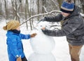 Little boy with his father building snowman in snowy park. Active outdoors leisure with children in winter. Kid during stroll in a Royalty Free Stock Photo